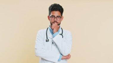 Hintli genç doktor kardiyolog umutsuzluk ve yalnızlık hissediyor, sinir krizi geçiriyor, kaybediyor, kötü şans, kayıp, kötü haber, başarısızlık. Arap eczacı, bej arka planda izole edilmiş.