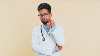 Gözüm üzerinde. Özgüvenli Hintli genç doktor kardiyolog gözlerini ve kamerasını işaret ederek birinin samimiyetini gözetliyor. Arap eczacı, bej arka planda izole edilmiş.