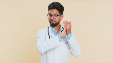 Aferin, aferin. Hintli genç kardiyolog gururla alkışlıyor ve onaylıyor, başarılı bir iş, tamam. Arap eczacı, bej arka planda izole edilmiş.