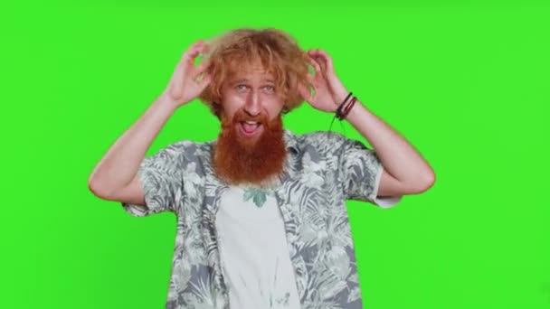 面白いおかしな遊び心のある若いひげの男は 愚かな表情と笑顔を作り 舌を示すこと ばかげた表現を馬鹿げている 緑色のクロマのキーバックで隔離された男 人々のライフスタイル — ストック動画