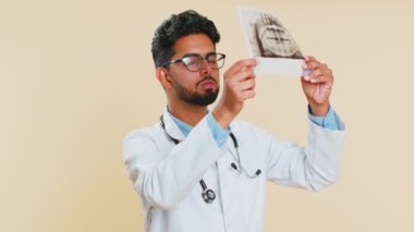 Hintli genç doktor ortodontist adam çene dişlerinin panoramik röntgen fotoğrafını inceliyor. Hasta ağzının 3 boyutlu modeli, MRI taraması. Diş hekimliği, oral bakım. Bej arka planda Arap stomatolojisi uzmanı.