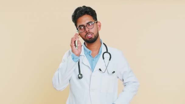焦虑不安焦虑不安疲惫的印度医生心脏病专家男人在两个手机上尖叫时 会引起对话冲突的争吵 基于米色背景被隔离的阿拉伯药师 — 图库视频影像