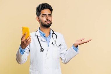 Hintli doktor kardiyolog akıllı telefon kullanarak boş yeri gösteriyor, reklam uygulaması alanı, olumlu geri bildirim, kopyalama alanı. Arap eczacı, bej arka planda izole edilmiş.