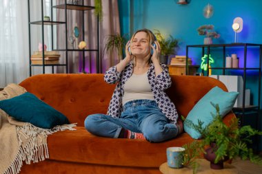 Kablosuz kulaklıklı mutlu kadın evinde koltukta oturup en sevilen enerjik disko dans müziğini seçiyor. Kafkasyalı kız hafta sonu eğlencesine çıkıyor..