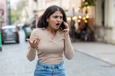 Kızgın kızgın, sinirli, Hintli genç bir kadın telefonda tartışırken sinirli, dışarıda bağırarak kavga ediyor. Hispanik, şehir caddesinde duran hoşnutsuz, kızgın kızı gücendirdi. Kasaba yaşam tarzları