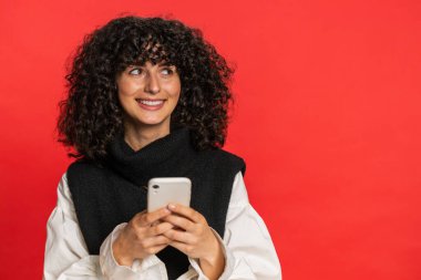 Beyaz bir kadının mesajlaşması akıllı telefon sosyal medya uygulamalarında içerik paylaşımı, rahatlama filmi izlemesi. Genç kız kırmızı arka planda izole edilmiş cep telefonu gülümsemesi kullanıyor.