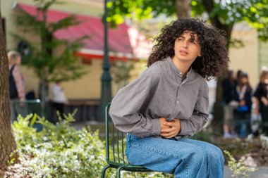 Dönem kramplarından muzdarip hasta genç bir kadın dışarıda karın ağrısı çekiyor. Karnında karın ağrısı hisseden bir kız şehir caddesinde oturuyor. Karın ağrısı gastrit. Güneşli park