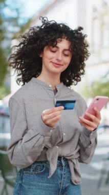 Kafkasyalı genç bir kadın kredi kartı akıllı telefonu kullanarak para aktarıyor, online alışveriş yapıyor, dışarıdan yemek siparişi veriyor. Şehir caddesindeki bayan kız. Dikey