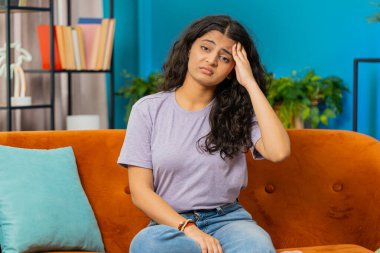 Hasta Hintli kadın baş ağrısı problemini tedavi etmek için tapınakları ovuyor, tansiyon, migren, stres, ekşitme, evde yüksek tansiyon. Kapalı bir odada kanepede oturan üzgün bir Arap kız.