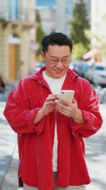 Asyalı orta yaşlı bir adam sosyal medya uygulamasında akıllı telefon kullanıyor, internette sörf yapıyor, dinleniyor, dışarıda mola veriyor. Şehir caddesinde yürüyen Çinli bir adam. Dikey