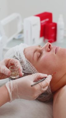 Yüz soyma maskesi, kaplıca güzellik tedavisi, cilt bakımı. Güzellik uzmanları genç kadın yüzüne nemlendirici krem sürüyor. Yüzü sulansın diye. Güzellik salonunda yaşlanma karşıtı kozmetik işlemler yapılıyor. Dikey