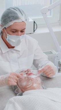 Yüz soyma maskesi, kaplıca güzellik tedavisi, cilt bakımı. Güzellik uzmanları genç kadın yüzüne nemlendirici krem sürüyor. Yüzü sulansın diye. Güzellik salonunda yaşlanma karşıtı kozmetik işlemler yapılıyor. Dikey