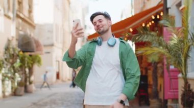 Neşeli blog yazarı akıllı telefondan selfie çekiyor abonelerle ya da aile dostlarıyla görüntülü iletişim kuruyor sosyal medya vlog 'u için hikayeler kaydediyor, el sallıyor. Şehir sokağındaki adam..