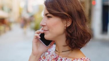 Uzaktan iletişim kuran mutlu kadın akıllı telefonla konuşuyor. Beyaz, genç, yetişkin bir kız telefonda konuşuyor. Şehir caddesinde beklenmedik bir dedikodu dolaşıyor. Şehir yaşam tarzları açık havada