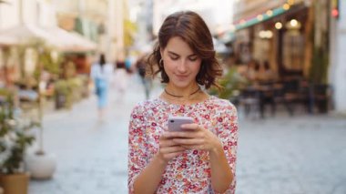 Akıllı telefon kullanarak gülümseyen genç bir kadın. Kısa mesajlar yazarak interneti tarıyor, işi bitiriyor, dışarıdaki kameralara bakıyor. Şehir caddesinde yürüyen bir kız turist. Kasaba yaşam tarzları