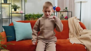 Modayı takip eden neşeli, pozitif sarışın çocuk dans ederek eğleniyor, ritme ayak uyduruyor, el kaldırıyor, dublaj yapıyor. Oturma odasında kanepede oturan Kafkas çocuk.
