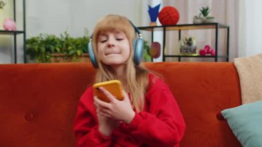 Kablosuz kulaklık takmış, koltukta oturup en sevilen enerjik disko dans müziğini dinleyen mutlu genç kız çocuk. Çocuklar hafta sonu eğlence aktiviteleri. Yaşam Tarzları