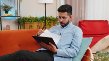 Mutlu Hindistanlı serbest çalışan adam evdeki koltukta belgelerle çalışıyor iş gazeteleri okuyor mali raporlar hazırlıyor. Genç İspanyol muhasebeci grafik belgelerini analiz ediyor, vergileri hesaplıyor..