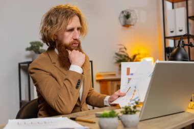 Beyaz sakallı serbest muhasebeci mali grafik belgeleriyle çalışıyor, çizelgeler için vergileri hesaplıyor ve ofis masasında raporlar hazırlıyor. Dizüstü bilgisayarda çalışan iş adamı, harcama bütçesi planlıyor..