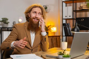 Genç işadamı ofis masasında oturuyor cep telefonuyla müşteriye cevap veriyor, akıllı telefon kullanıyor. Sohbet. Kafkas sakallı adam uzaktan kumanda işinde çalışıyor, konuşuyor..