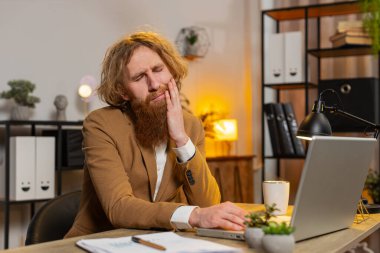 Diz üstü bilgisayarda çalışan, diş ağrısı çeken diş ağrısı çeken, diş hastalığından dolayı acı veren bir yüz ifadesi olan kızıl saçlı iş adamı. Taşıma, pulpitis, sakız hastalığı, diş hastalıkları konsepti.