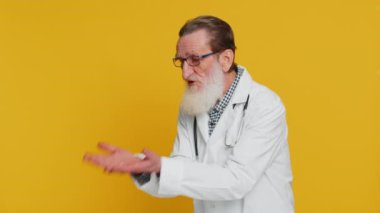 Kıdemli yaşlı doktor kardiyolog elini kaldırarak sorunların neden şüphe uyandırdığını soruyor. Eczacı eczanesi. Yaşlı büyükbaba sarı arka planda izole edilmiş.