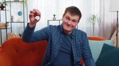 Yeni ev dairesinin anahtarlarını gösteren mutlu beyaz erkek emlakçı, emlak satın alma veya kiralama, ipotek kredisi, modern ev odası dairesine yatırım. Koltukta oturan gülümseyen adam..