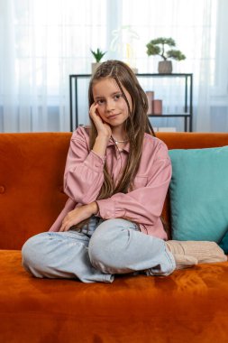 Mutlu gülümseyen genç kız çocuğunun portresi rahat koltukta oturup evdeki oturma odasındaki kameraya bakıyor. Kahverengi uzun saçlı, tatlı, genç bir kız öğrenci. Yaşam Tarzları.
