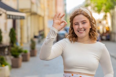 - Tamam. Neşeli, kızıl saçlı genç bir kadın kameraya bakıyor. İyi bir jest yapıyor, olumlu bir işaret veriyor. Güzel bir şey onaylıyor, dışarıda galibiyeti kutluyor. Şehir caddesinde kızıl saçlı kız