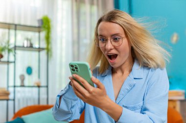 Aman Tanrım. Vay canına. Heyecanlı mutlu, neşeli, serbest çalışan genç bir kadın akıllı telefon kullanarak ekranda kutlama yaparak iyi haber kazanıyor. Rüzgarlı saçlı iş kadını telefonda konuşuyor..