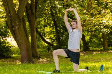 Sportif formda bir adam parkta yoga yaparken spor minderinde nefes egzersizi yapıyor. Ellerinizi kaldırın. Koşucu dışarıda egzersiz yapmaktan hoşlanıyor. Aktif sporcu motivasyonu. Aktif sporcu sağlıklı yaşam tarzı.