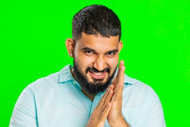 Sinsi kurnaz Hintli genç adam hileli yüz hareketleriyle ve şeytani planlarıyla sinsi kötü adam fikrini, hilekarlığını, şakalarını, şakalarını düşünüyor. Yeşil krom anahtar arka planında izole edilmiş bir Arap.