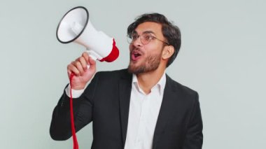 Hintli işadamı megafonla konuşuyor, haberleri duyuruyor, reklam indirimlerini yüksek sesle duyuruyor, konuşma yapmak için hoparlör kullanıyor. Stüdyo gri arka planda izole edilmiş mutlu Arap adam.