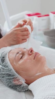 Kozmetik doktoru kadın yüzü, spa salonundaki pamuklu mendillerle boynu temizliyor. Kız teninin kozmetik güzellik prosedüründen önce temizlenmesi. Güzellik uzmanından yüz bakımı. Dikey yakın plan portre