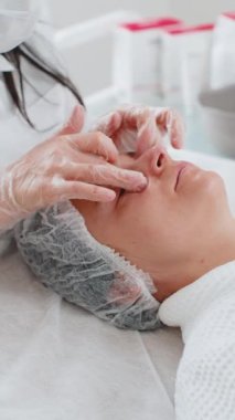 Terapist kadın, elleriyle spa masajı yaptırıyor. Salonda pürüzsüz, sağlıklı cilt bakımı. Göz altı torbaları iyileşiyor. Yüz fizyolojisi seansında müşteri. Dikey çekim