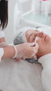 Güzellik uzmanı kadın yüzüne nemlendirici asit serumu uyguluyor. Gözlerin etrafındaki narin cildin gençleşmesi. Yaşlanma önleyici tedavi kırışıklıkları, siyah halkaları, torbaları, tansiyon eksikliğini, kuruluğu ortadan kaldırıyor.