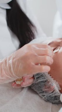 Güzellik uzmanı kadın yüzüne nemlendirici asit kokteyli sürüyor. Gözlerin etrafındaki narin cildin gençleşmesi. Yaşlanma önleyici tedavi kırışıklıkları, siyah halkaları, torbaları, tansiyon eksikliğini, kuruluğu ortadan kaldırıyor.