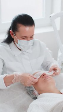 Güzellik uzmanı kadın yüzüne nemlendirici nano maske uyguluyor. Gözlerin etrafındaki narin cildin gençleşmesi. Yaşlanma önleyici maske tedavisi kırışıklıkları, siyah halkaları, torbaları, tansiyon eksikliğini, kuruluğu ortadan kaldırıyor.