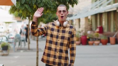 Neşeli genç turist, kameraya gülümseyen, el sallayan, el sallayan davetkar merhaba, merhaba, merhaba, güle güle, misafirperver bir yüz ifadesiyle hoş geldiniz. Şehir merkezindeki adam..