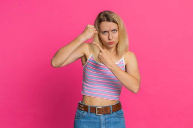 Saldırgan, kızgın, beyaz, 30 yaşında genç bir kadın kameraya karşı dövüşmeye çalışıyor, yumruklarını sallıyor, ifadeyle boks yapıyor, cezalandırıyor, tehdit ediyor, taciz ediyor, öfkeden kuduruyor. Pembe arka planda izole edilmiş kız