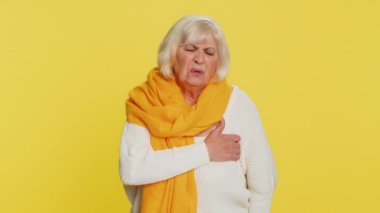 Stresli, korkmuş, yaşlı bir kadın, kalp krizi geçirmiş, kalp krizi geçirmiş, kalp krizi geçirmiş, kalp krizi belirtileri gösteren, kendini hasta hisseden bir kadın. Sarı arka planda yaşlı, olgun bir büyükanne.