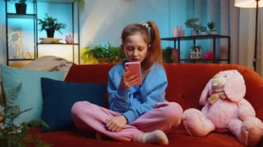 Küçük kız akıllı telefon kullanıyor, oyun oynuyor, beklenmedik piyango sonuçlarını kaybediyor, kötü haber, servet kaybı, başarısız eğitim sınavı. Akşam odasındaki genç kız kanepede oturuyor.