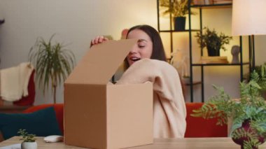 Evde oturan mutlu beyaz kadın teslimat paketini açıyor. Gülümseyen kız alışverişci, çevrimiçi dükkan müşterisi karton kutu açıyor posta yoluyla hediye kulaklıkları alıyor