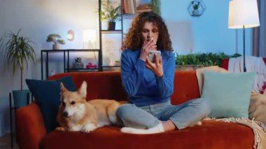 Oturma odasındaki kanepede Corgi Dog 'un yanında oturan kıvırcık saçlı huysuz kadın akıllı telefon kullanıyor. Günlük kıyafetli genç kız kaybediyor ve piyango ya da kötü haber karşısında şaşırıyor..