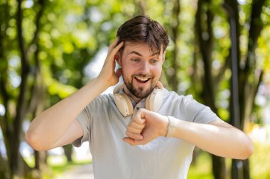 Şehir parkında koşan ve akıllı sineklere bakan mutlu koşucu. Heyecanlı adam spor takip cihazı kullanıyor ve başarıyı kutlayan sonuçları kontrol ediyor. Sporcu çocuk antrenman sonuçlarından memnun..