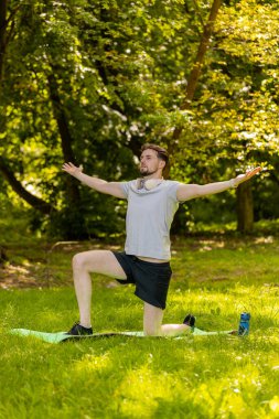 Sportif formda bir adam parkta yoga yaparken spor minderinde nefes egzersizi yapıyor. Ellerinizi kaldırın. Koşucu dışarıda egzersiz yapmaktan hoşlanıyor. Aktif sporcu motivasyonu. Aktif sporcu sağlıklı yaşam tarzı.