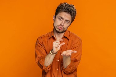 Biraz daha, lütfen bana ver. Kafkasyalı bir adam küçük bir jest yapıyor. Şüpheci bir gülümsemeyle minimum işaret veriyor. Küçük boyutta yalvarma yardımı alıyor. Yakışıklı adam turuncu stüdyo geçmişinde izole edilmiş.