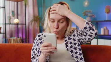 Heyecanlı genç bayan kazananın elinde akıllı telefon tutarak online bahis oyununun kazanmasıyla hayrete düşen iyi haberleri okumasına şaşırdım. Kanepede oturan mutlu Kafkasyalı kız evdeki zafer başarısından çok mutlu bir şekilde ekrana bakıyor.