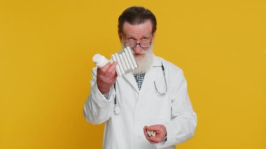 Kıdemli doktor kardiyolog, kabarcıklarda bir sürü hap olduğunu gösteriyor. İlaç, vitamin, antibiyotik tedavisi öneriyor. Sağlık hizmetleri. Eczacı dedesi sarı arka planda izole edilmiş.