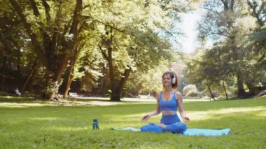 Lotus pozisyonunda oturan genç bir kadın yaz günü parkta dinleniyor. Sportif kaygısız yetişkin kız yoga meditasyonu yapıyor, pozitif enerji alıyor, sağlıklı yaşam tarzı. Aktif sporcu kadın.